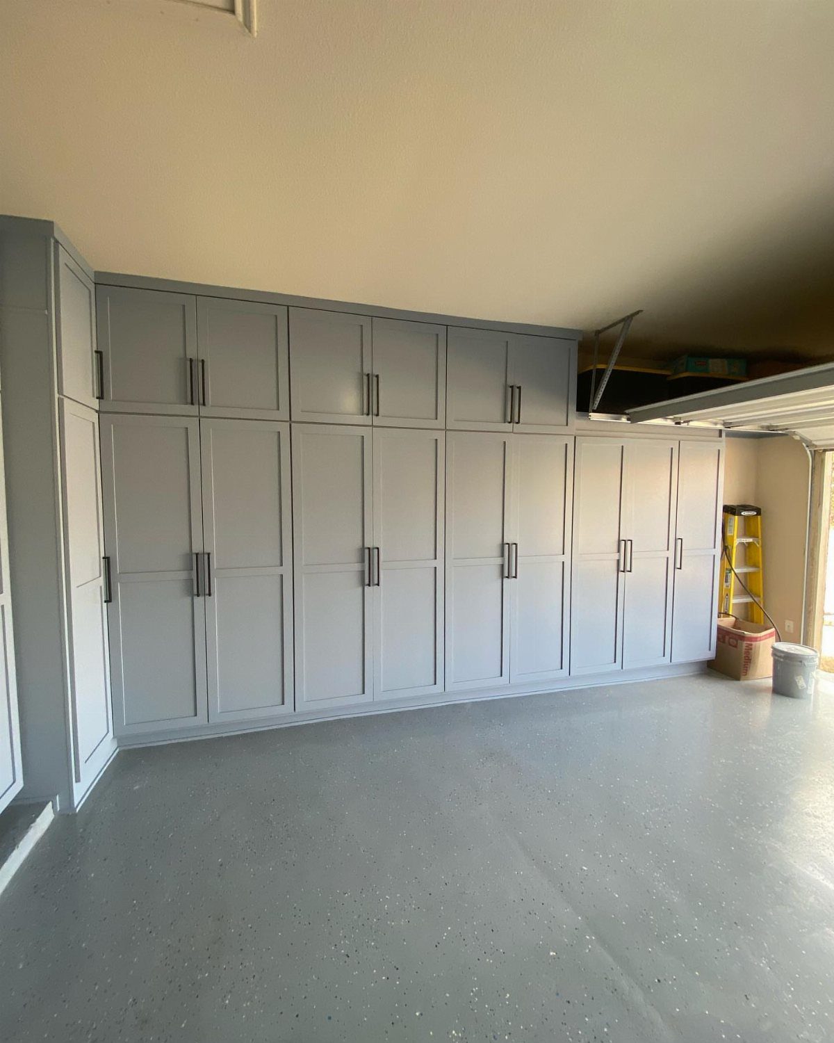 Light grey custom storage cabinets installed along a garage wall with a grey epoxy floor.