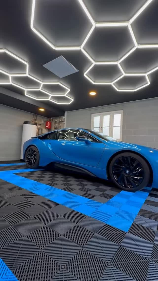 Blue sports car parked in a modern garage with hexagonal ceiling lights and patterned flooring.