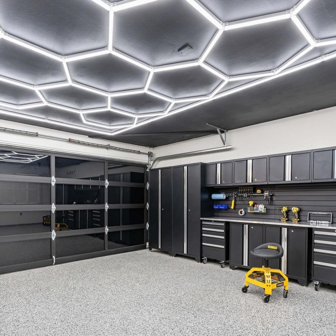 Hexagonal LED light strips integrated into a dark garage ceiling above black cabinetry and epoxy flooring.