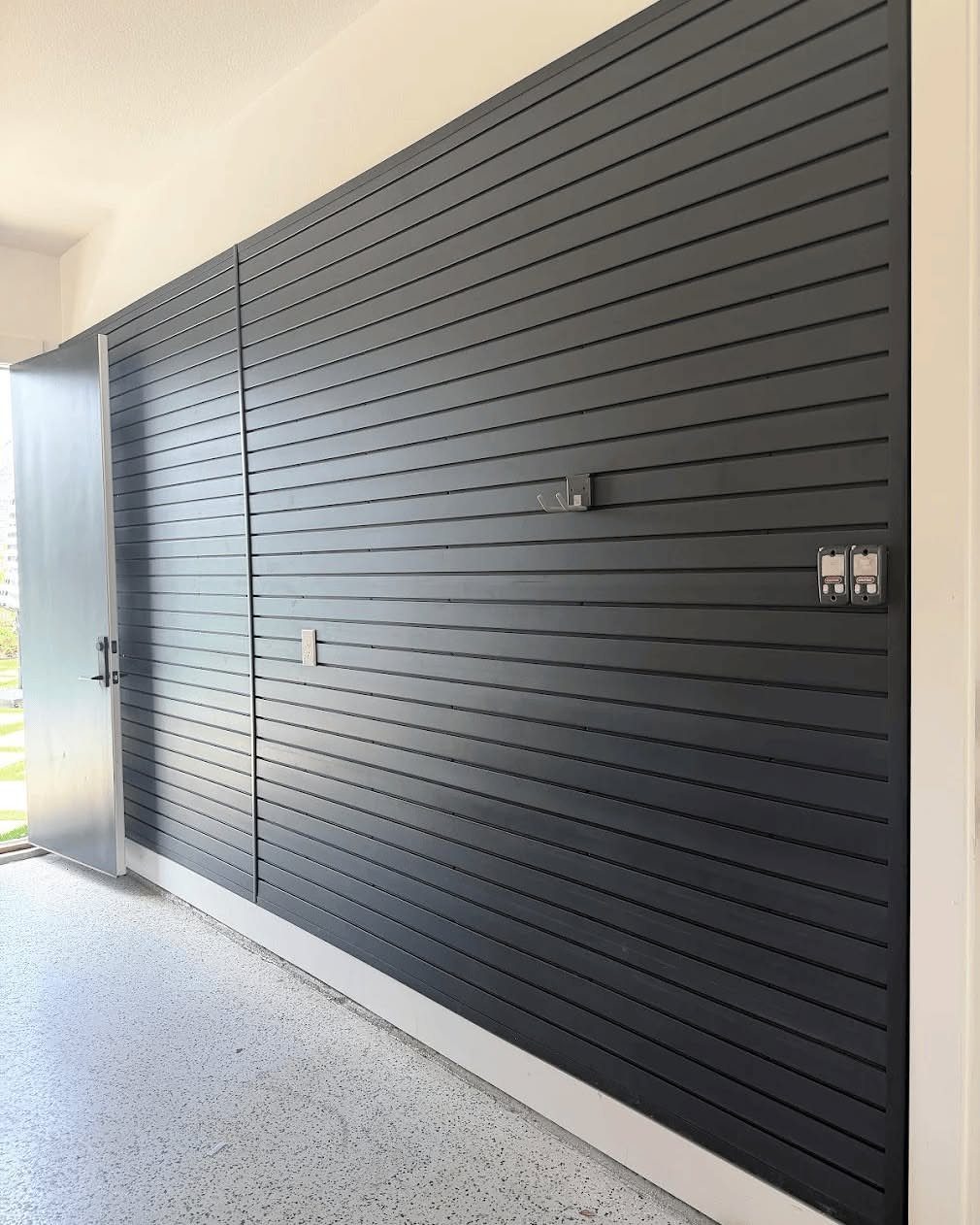 Dark grey slatwall system installed on a garage wall above an epoxy floor.