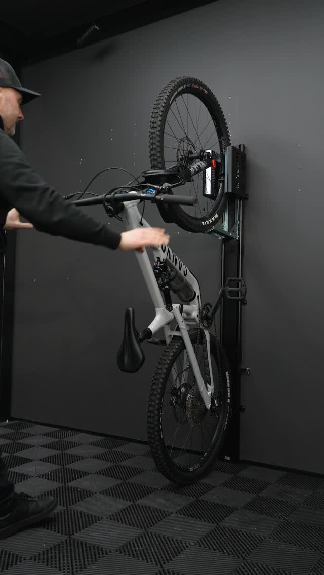 A man mounting a white mountain bike onto a vertical wall rack in a dark garage.