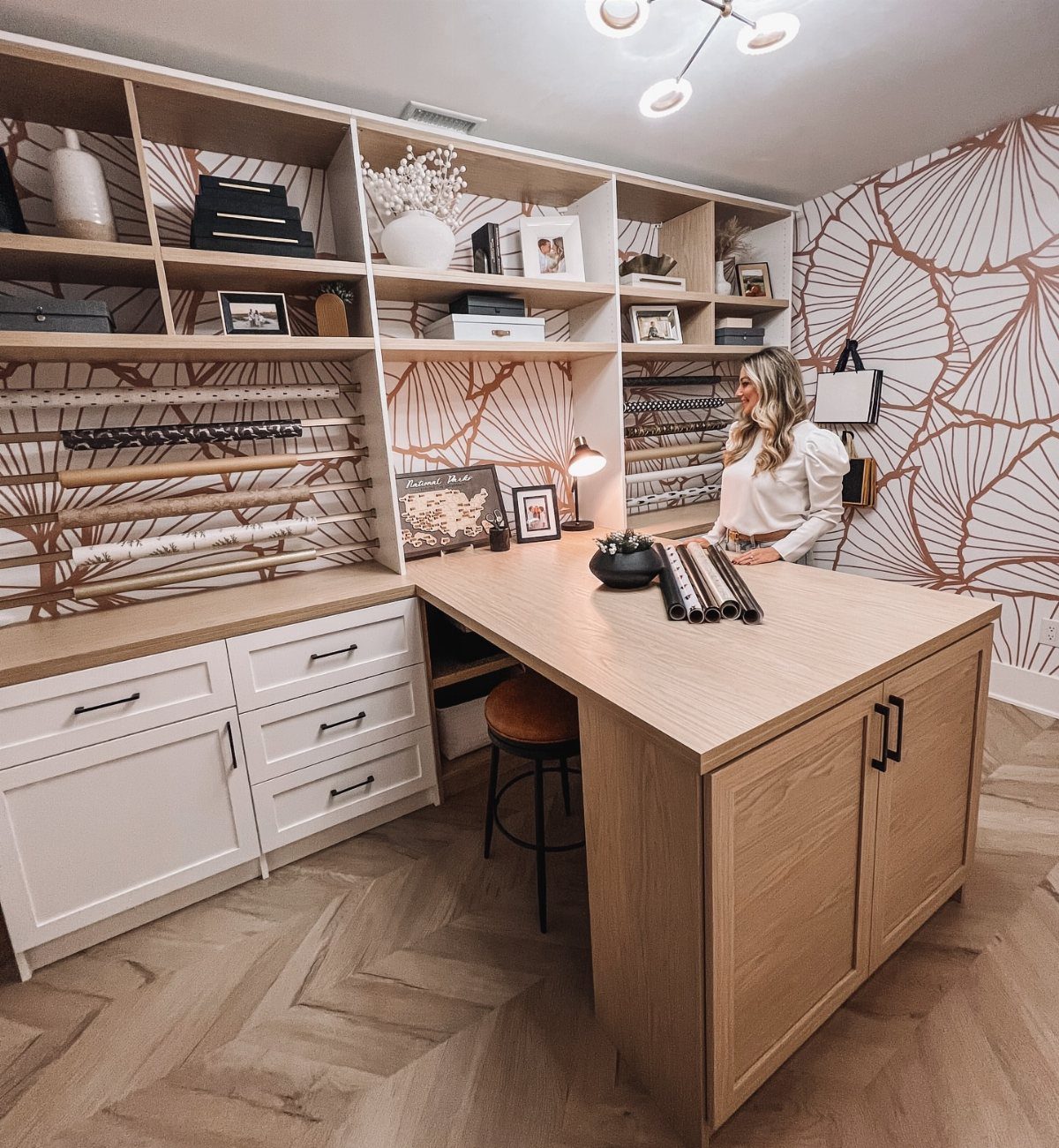 Garage to Family Room Conversion: 9 Ideas for 2026 5 A woman standing in a bright, organized craft room with large wooden workspaces and white cabinetry.