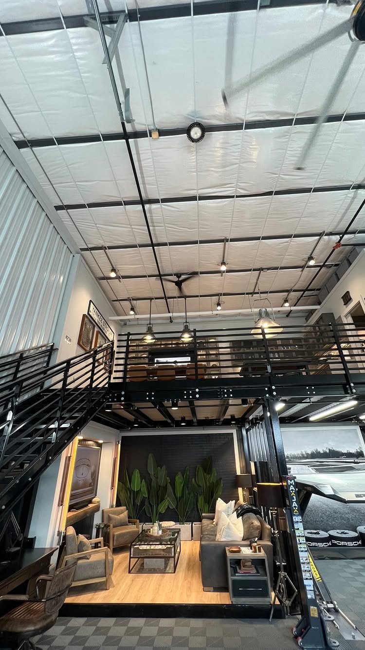 Garage to Family Room Conversion: 9 Ideas for 2026 7 Modern living room with mezzanine level and black metal staircase inside a converted high-ceilinged structure.