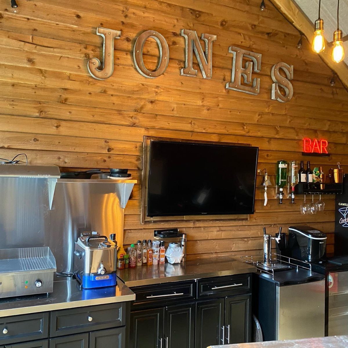 Garage to Family Room Conversion: 9 Ideas for 2026 3 Wooden paneled wall with metal letters spelling JONES above a bar with a television.