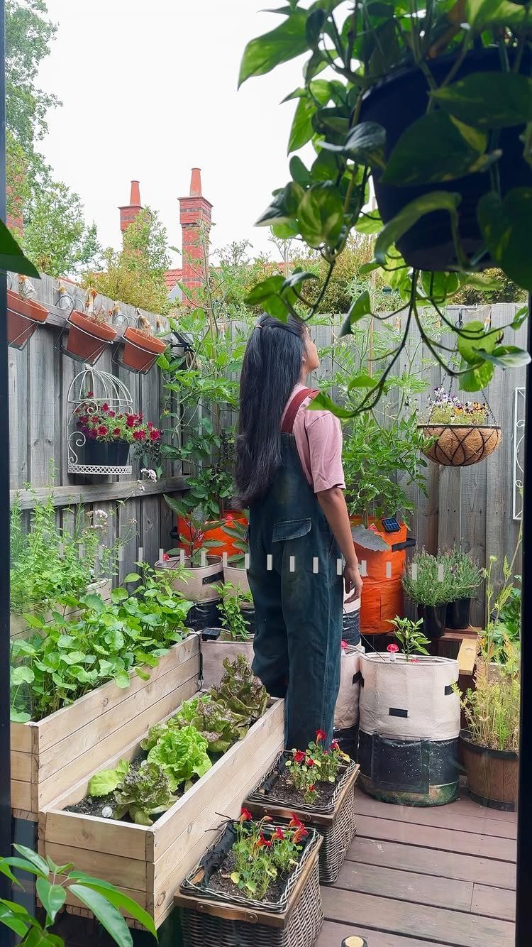 A person standing amidst many potted plants in a small, narrow wooden deck garden area.