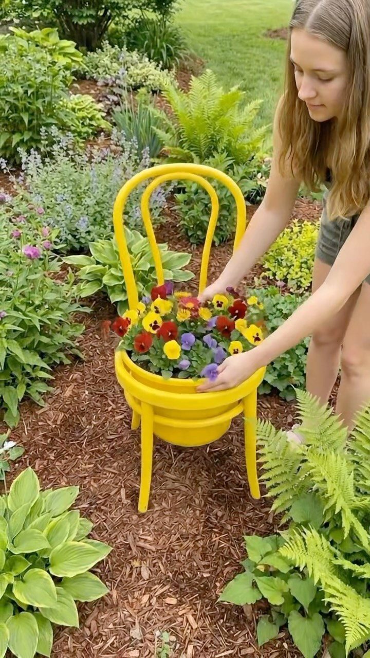 A young girl arranging colorful pansies inside a bright yellow metal chair planter in a garden.