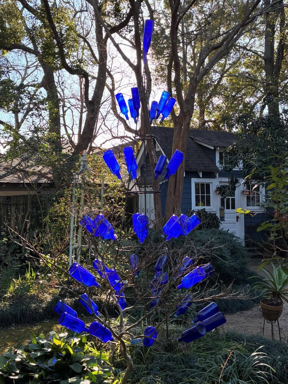 21 Home Decor Ideas for Garden Spaces That Work in Any Yard 14 Blue glass bottles attached to a metal frame forming a decorative bottle tree in a garden.