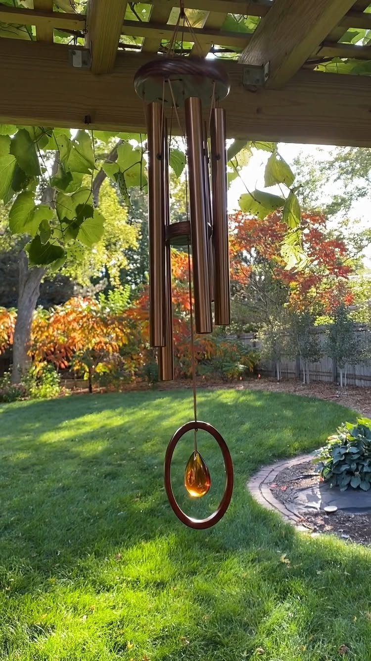 21 Home Decor Ideas for Garden Spaces That Work in Any Yard 7 Copper metal wind chimes with a glass teardrop hanging from a wooden pergola over a garden.