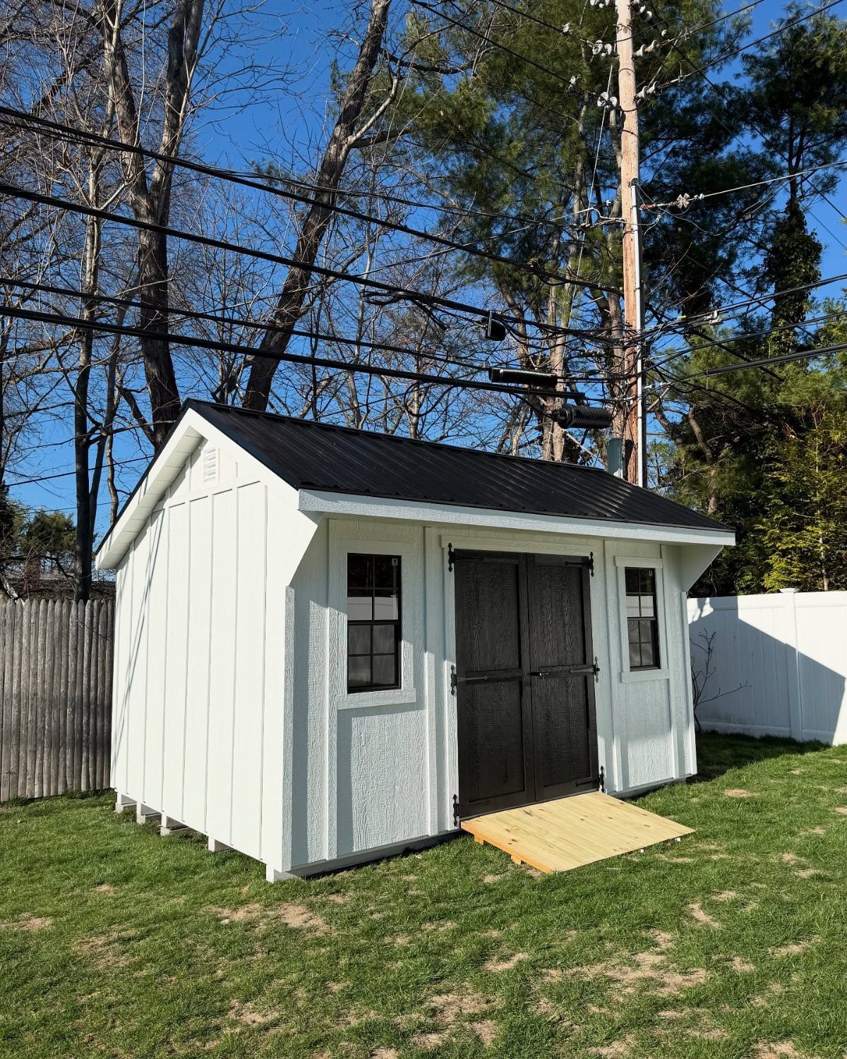 9 Modern Farmhouse Shed Ideas for 2026 7 A white wooden garden shed with black doors and a black metal roof on grass.