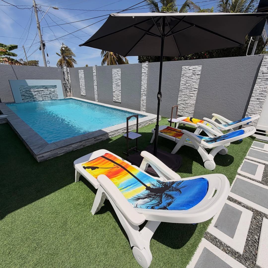 Pool Deck Ideas: 20 Designs From Breeze Blocks to Mountain Views 14 White lounge chairs with tropical prints sit on green turf beside a blue swimming pool.