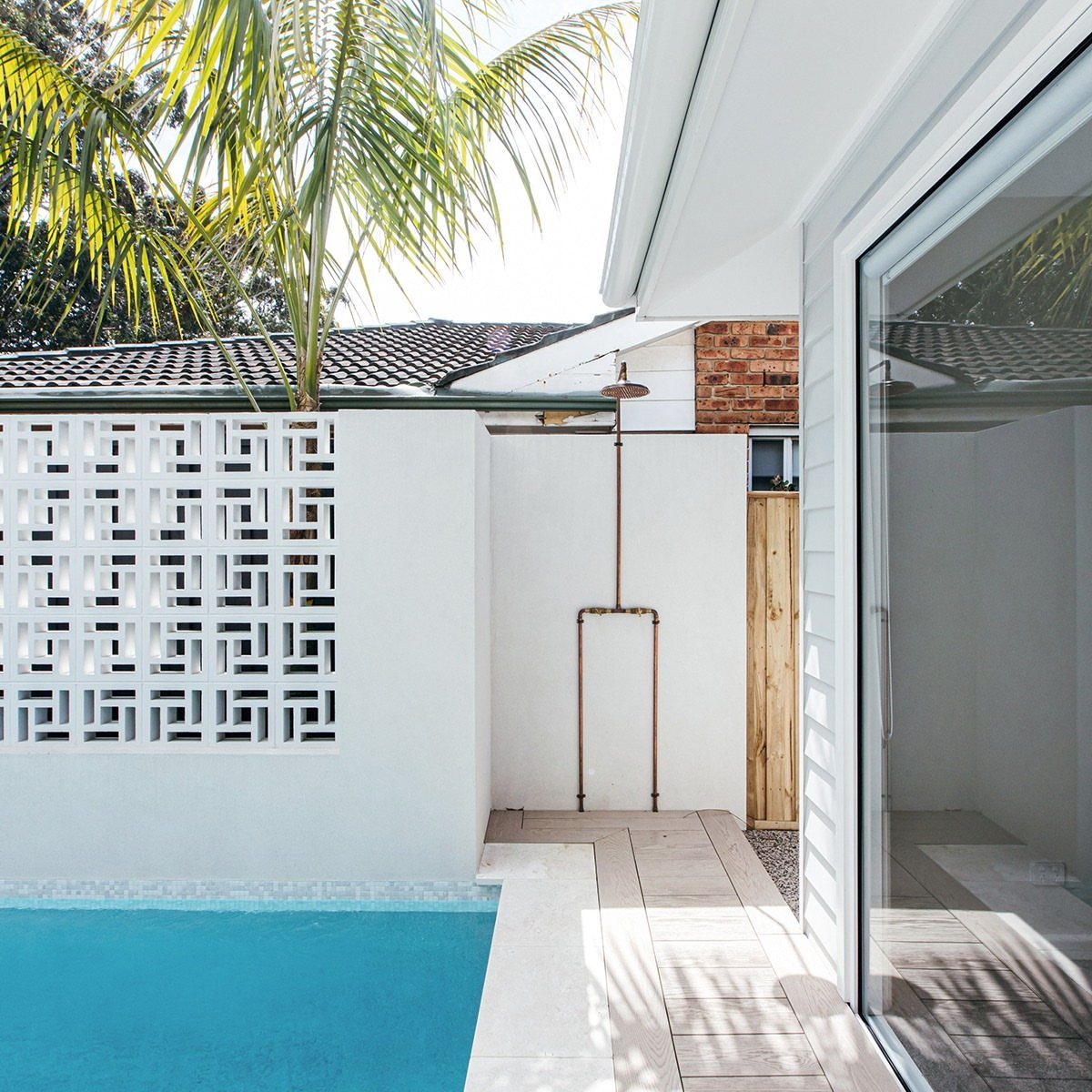 Pool Deck Ideas: 20 Designs From Breeze Blocks to Mountain Views 19 Modern pool area with light wood decking, blue water, and a white decorative breeze block wall.