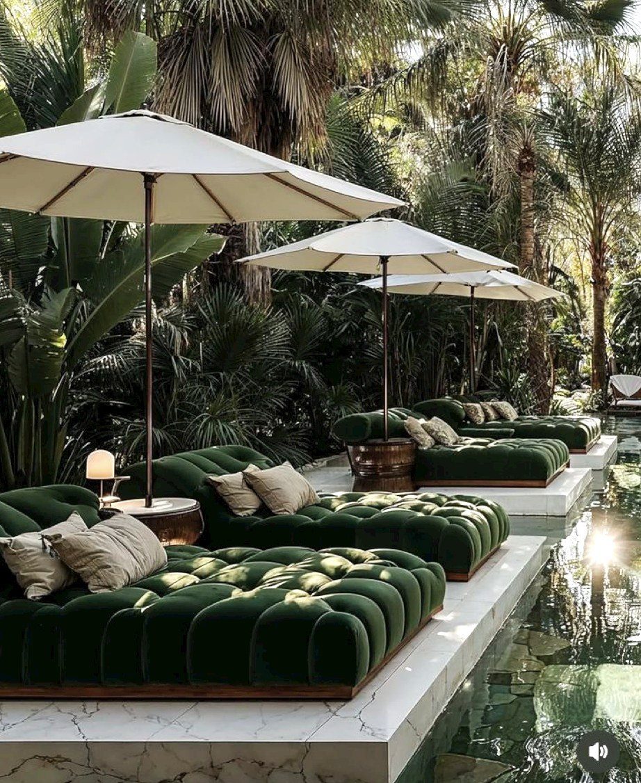 Pool Deck Ideas: 20 Designs From Breeze Blocks to Mountain Views 1 Green velvet tufted daybeds with white umbrellas arranged beside a marble pool in a tropical garden.