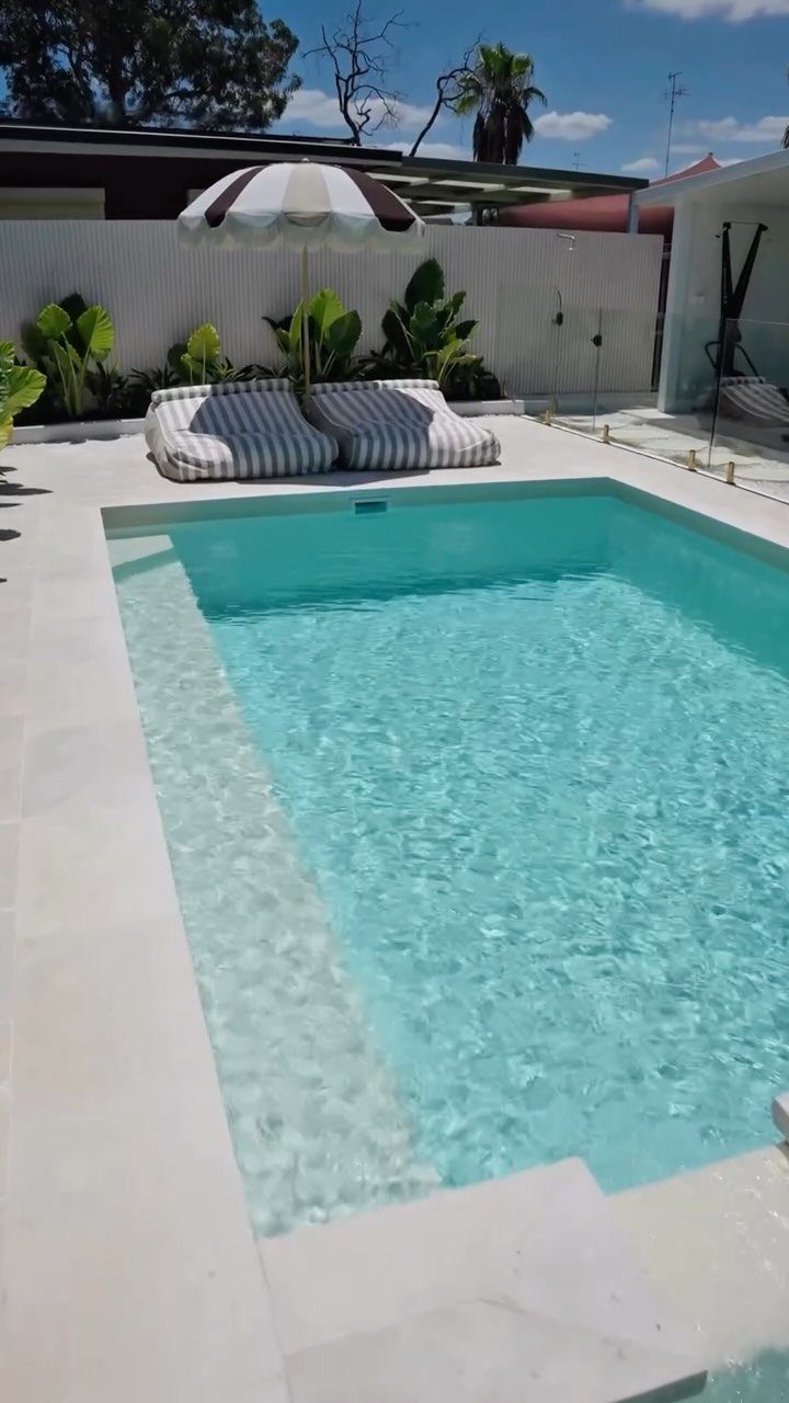 Pool Deck Ideas: 20 Designs From Breeze Blocks to Mountain Views 16 A rectangular swimming pool with turquoise water surrounded by a light stone deck and lounge chairs.