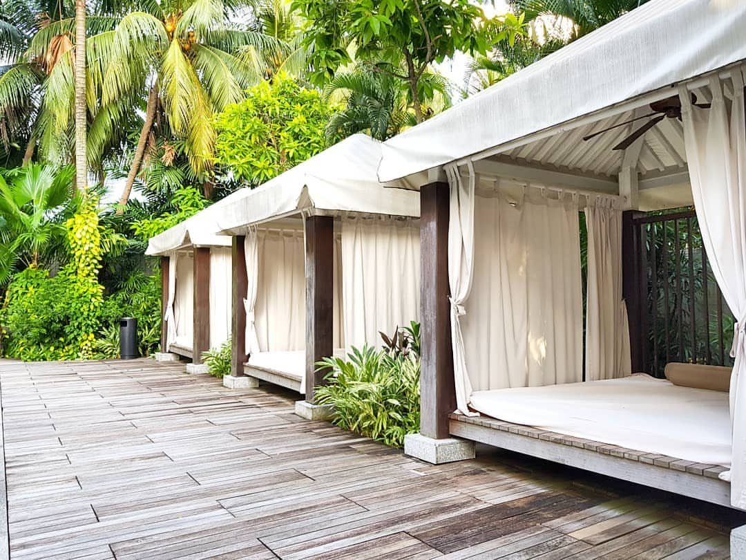 Pool Deck Ideas: 20 Designs From Breeze Blocks to Mountain Views 5 Three white canopy cabanas with wooden frames arranged on a wooden deck near tropical trees.