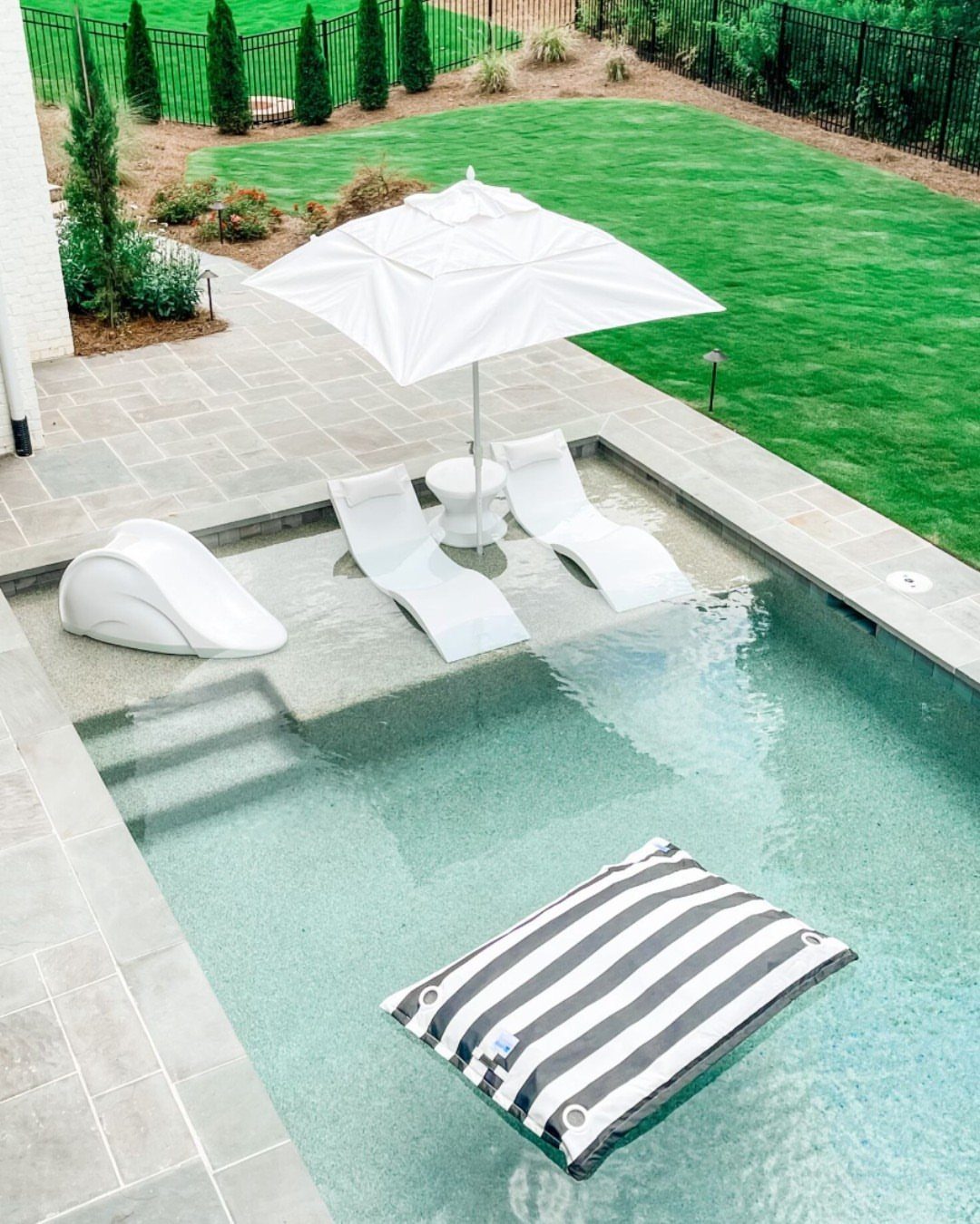 Pool Deck Ideas: 20 Designs From Breeze Blocks to Mountain Views 11 White lounge chairs under a patio umbrella in a stone-tiled swimming pool.
