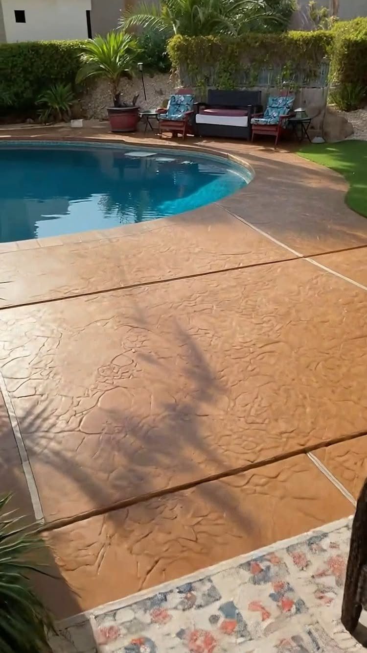 Pool Deck Ideas: 20 Designs From Breeze Blocks to Mountain Views 4 Terracotta stamped concrete pool deck surrounding a blue swimming pool with lounge chairs in the background.