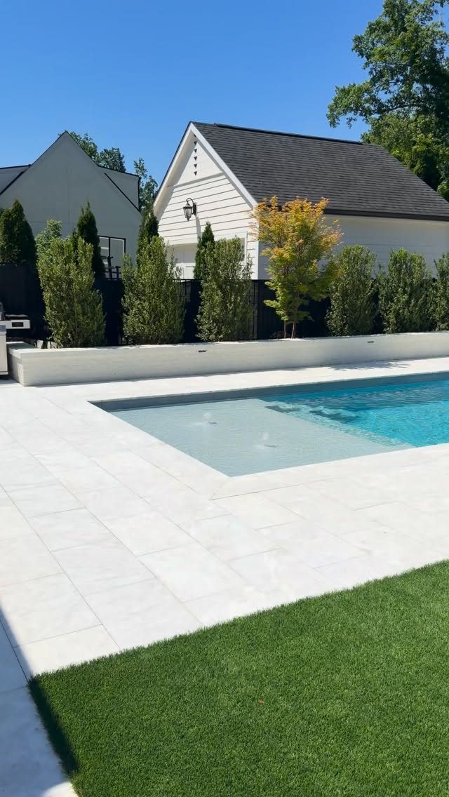 Pool Deck Ideas: 20 Designs From Breeze Blocks to Mountain Views 15 A modern swimming pool with white tiled decking and a green lawn in the foreground.