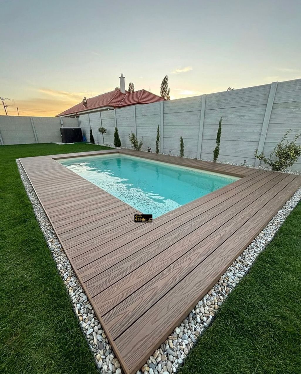 Pool Deck Ideas: 20 Designs From Breeze Blocks to Mountain Views 18 A rectangular swimming pool surrounded by a brown wooden deck and white pebbles on a green lawn.