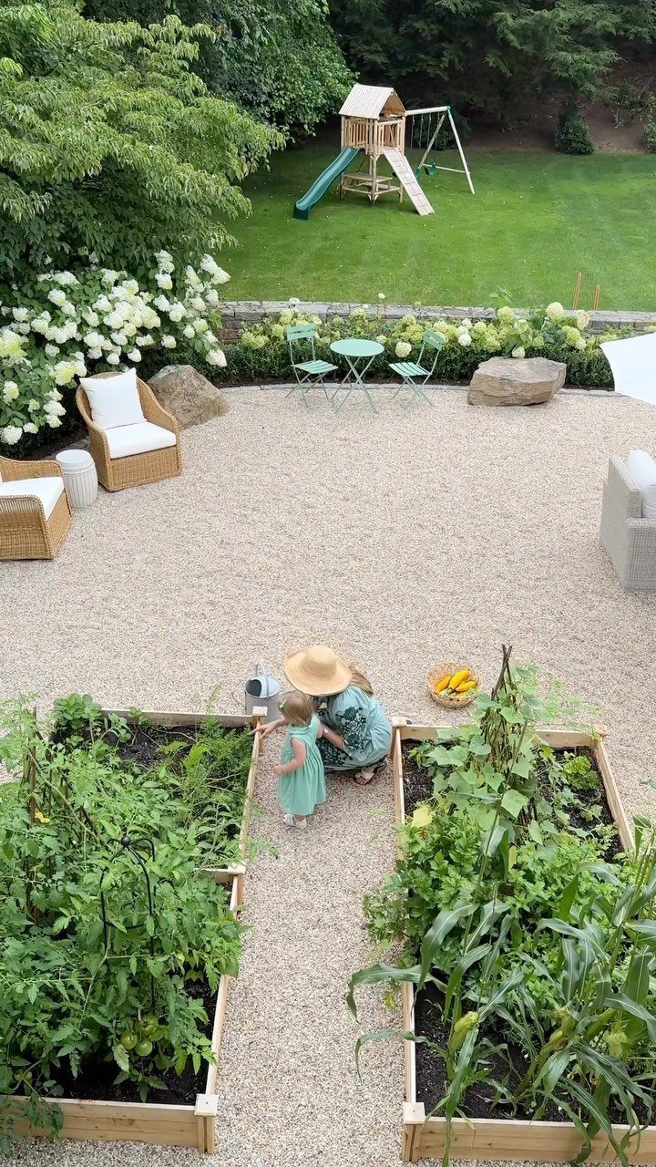 A woman and child tending to wooden raised garden beds surrounded by light pea gravel.