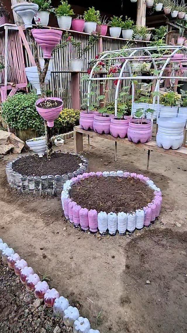 Circular raised garden beds constructed from pink and white painted plastic bottles filled with dark soil.