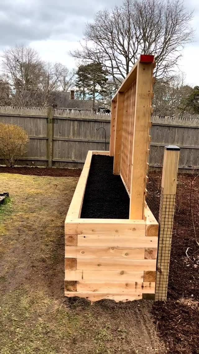 Raised Garden Beds: 9 Ideas for Materials, Layout and Drainage 2 A long wooden raised garden bed filled with dark soil stands in a backyard near a fence.