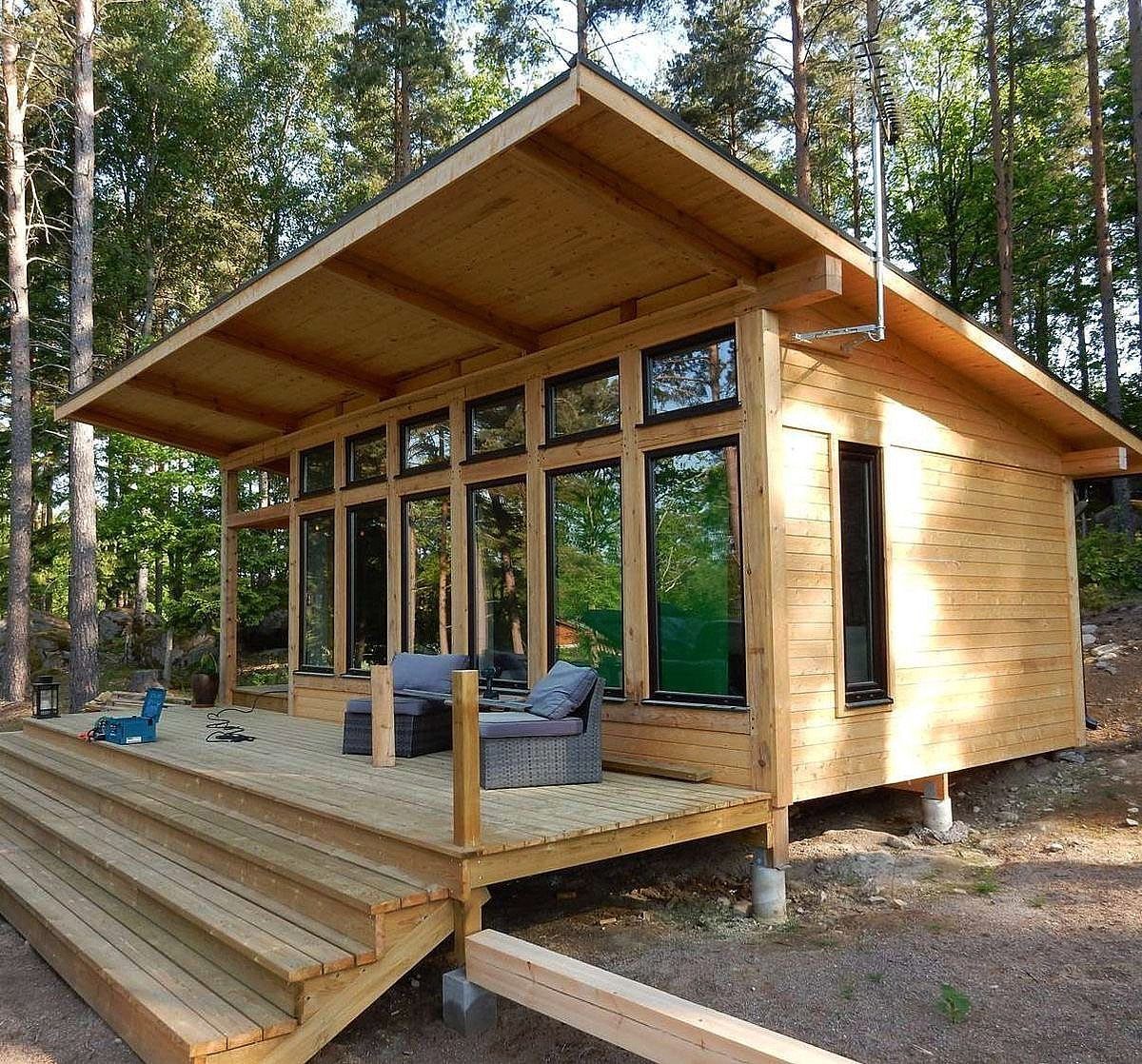 A modern wooden tiny house with large windows and a deck in a forest.