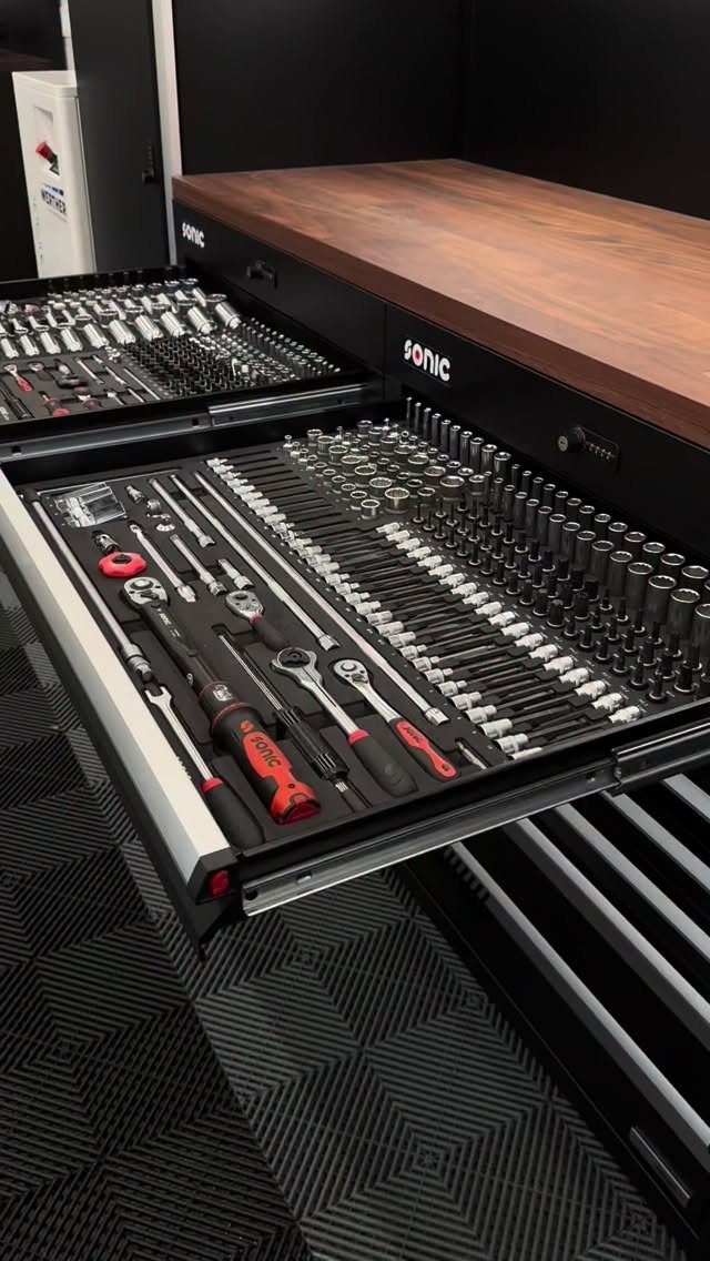 Open black tool chest drawers containing organized metal wrenches, sockets, and various hand tools.