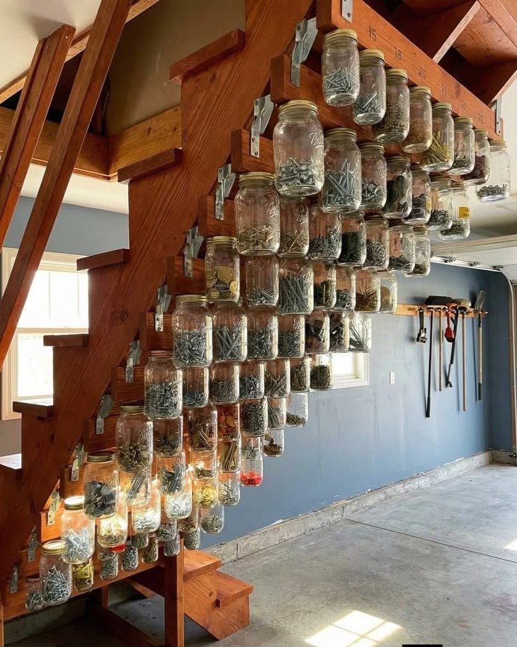 Glass jars filled with hardware items mounted along the side of a wooden staircase.