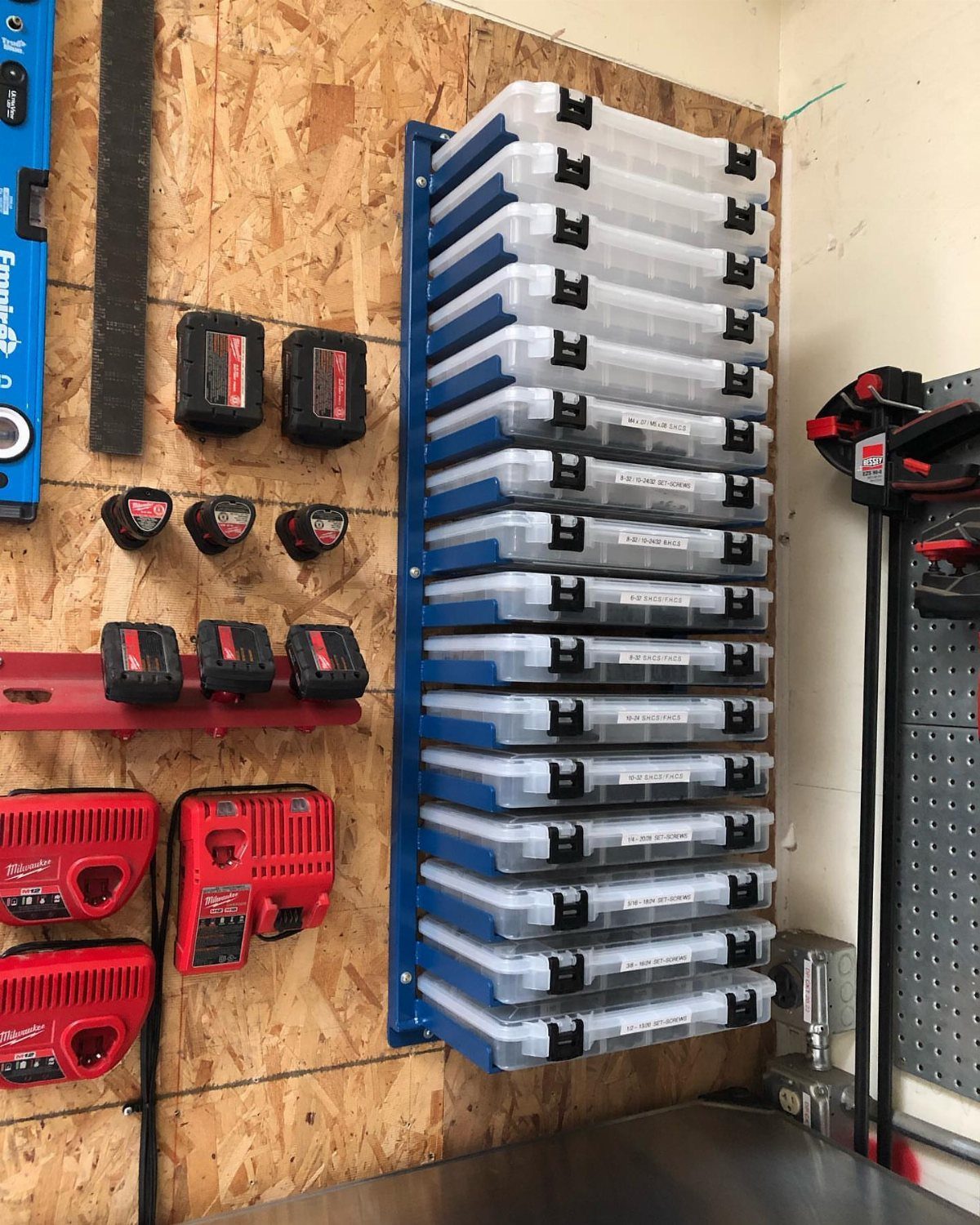 Clear plastic storage bins stacked vertically on a blue wall-mounted rack in a workshop.
