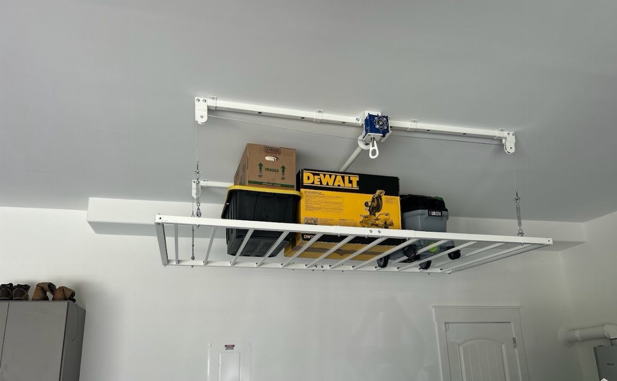 White metal overhead storage rack mounted to a ceiling holding various storage bins and boxes.