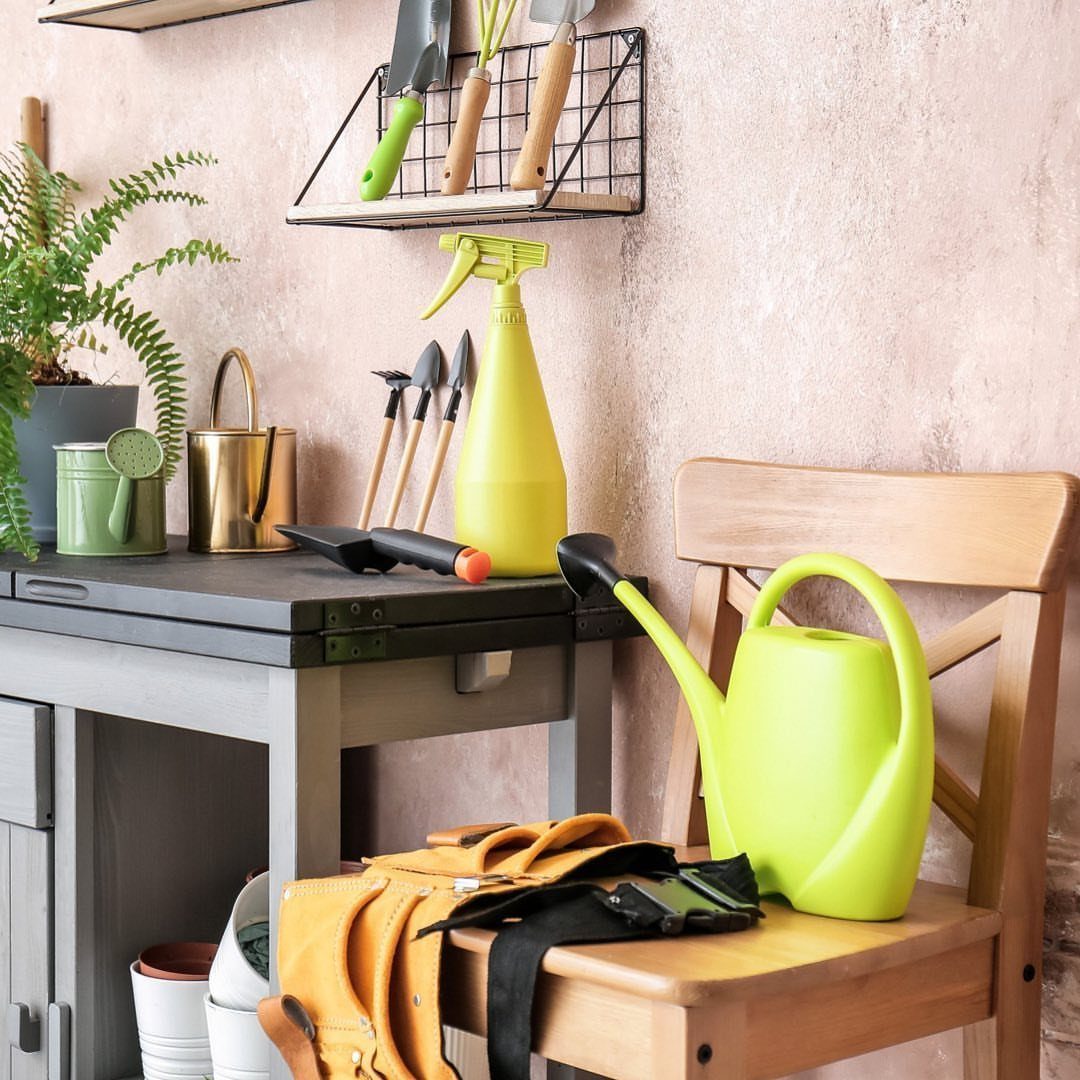 Gardening tools organized in a black wire wall basket above a grey workbench.