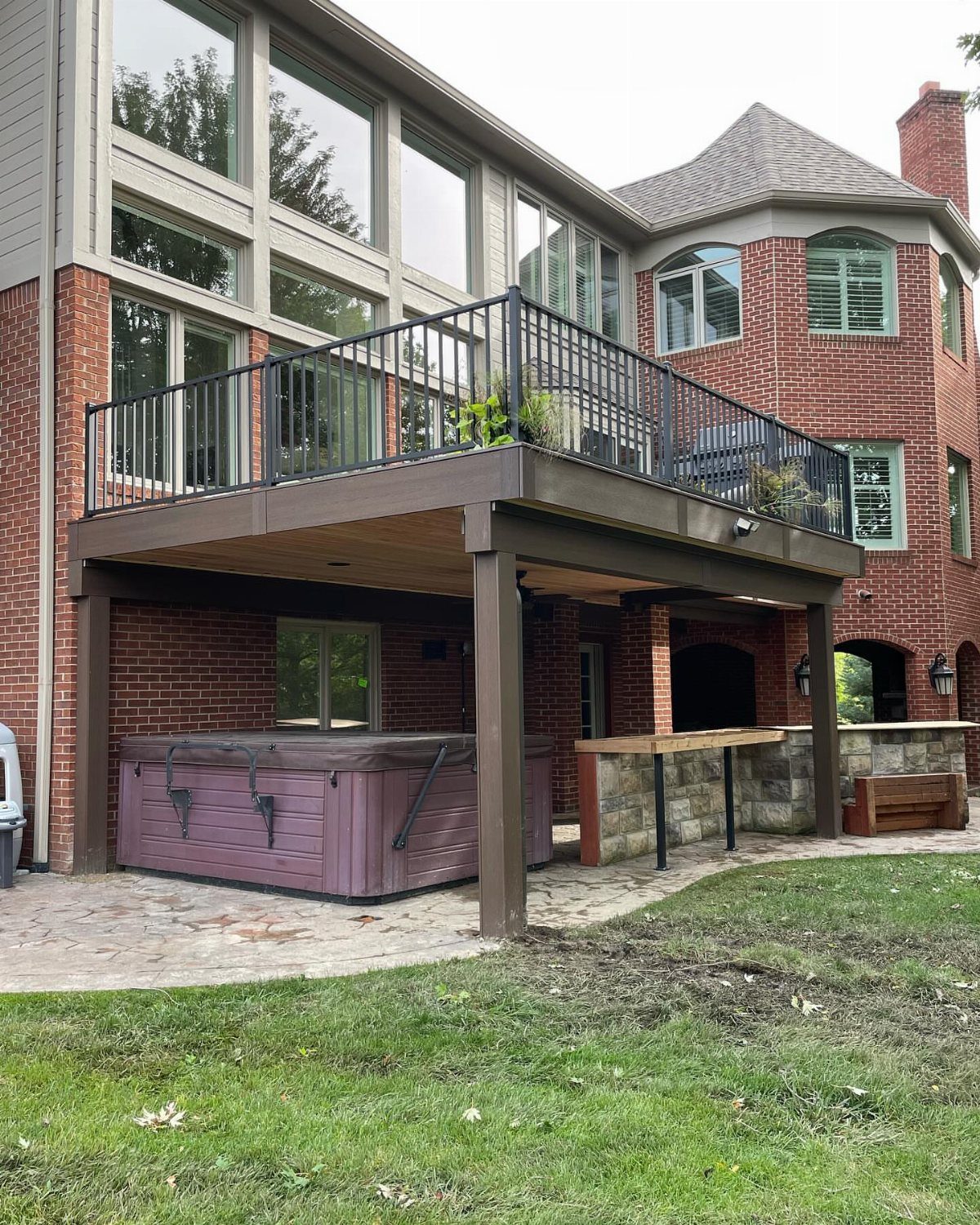 A purple hot tub sits on a stone patio under a large wooden deck structure.