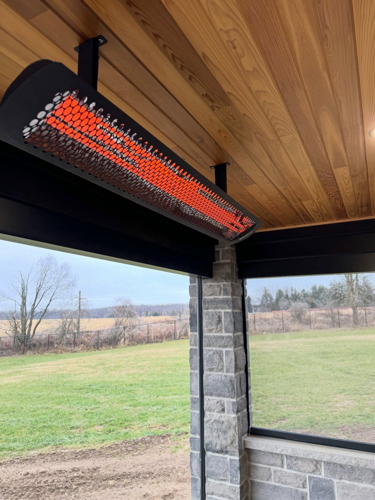 An infrared heater with glowing orange elements mounted to a wooden ceiling under a patio structure.