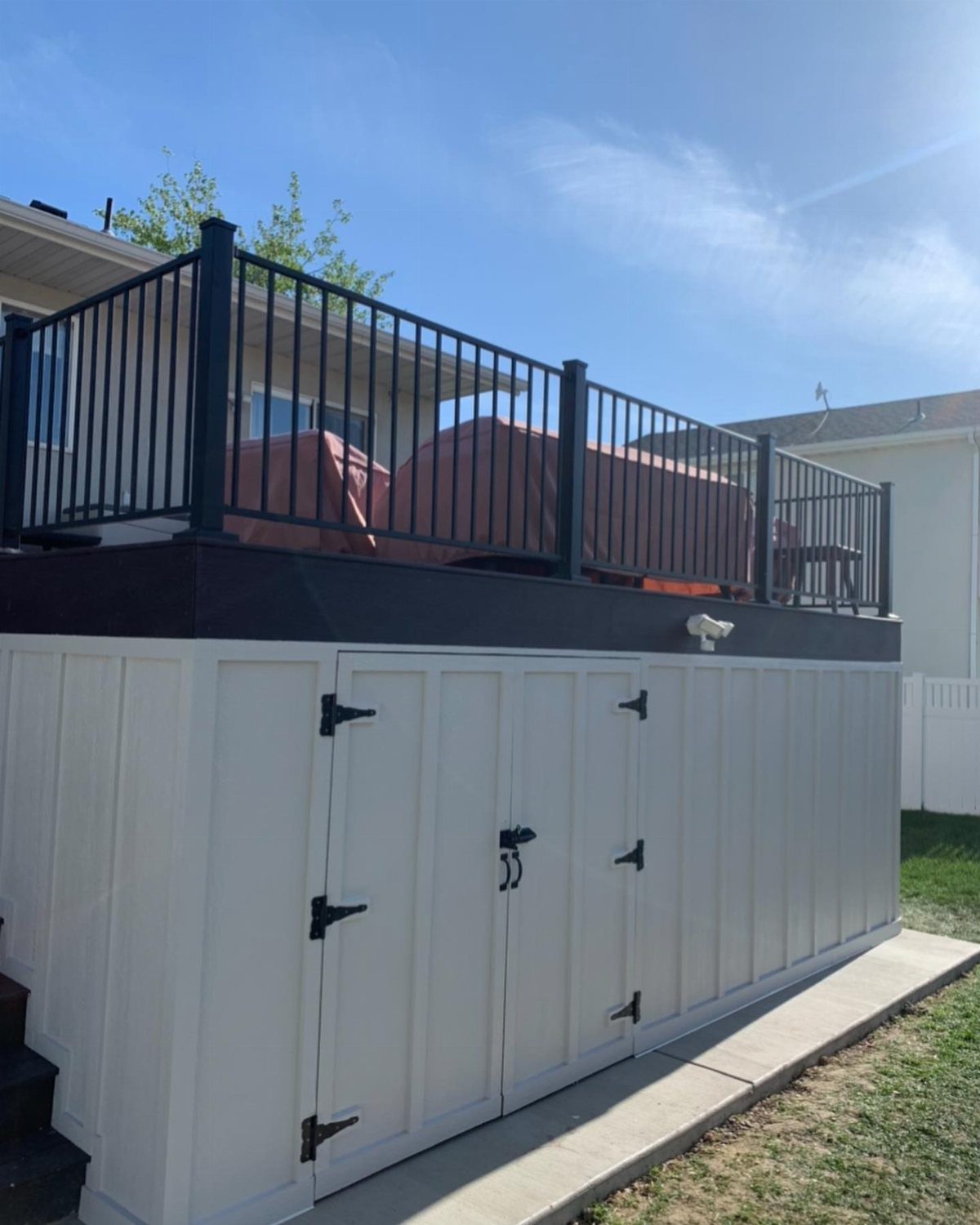 White storage doors built into the space underneath a raised wooden deck with black railings.