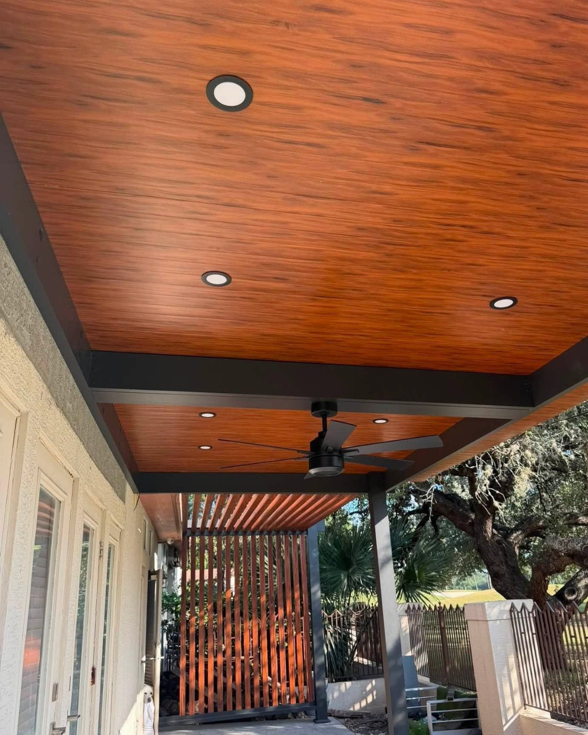 Polished reddish-brown wood plank ceiling with recessed lights and a black ceiling fan installed underneath.