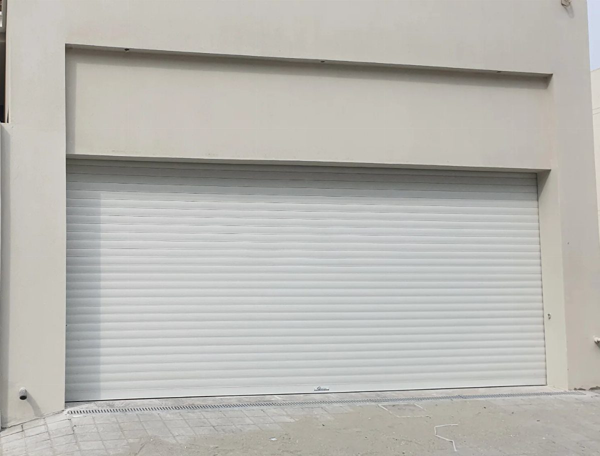 A wide, bright white rolling garage door installed in a light-colored building wall.
