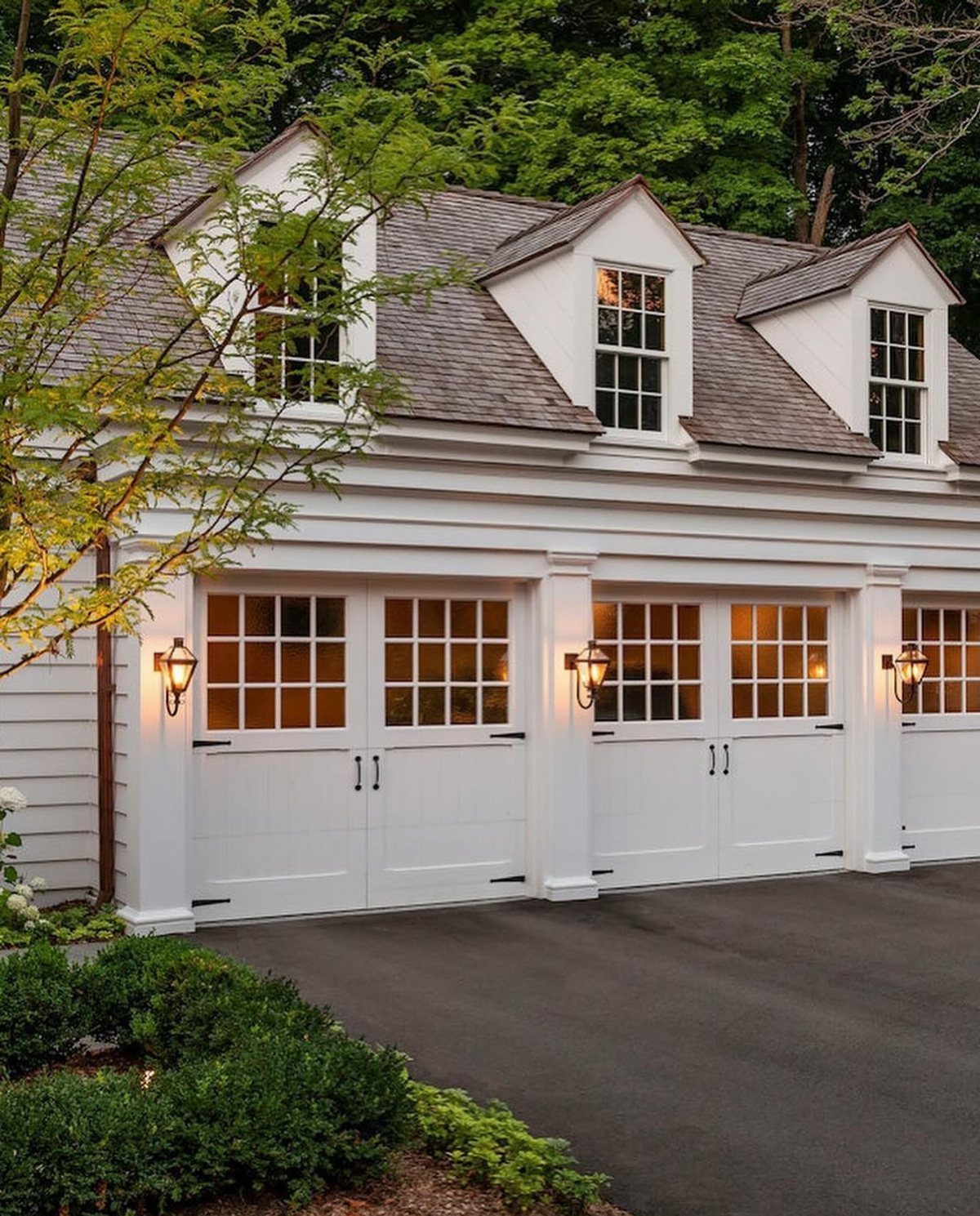White carriage house style garage doors with windows and black hardware under a shingled roof.