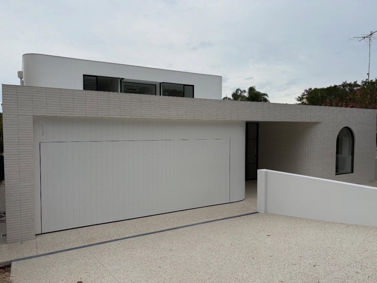 A wide white garage door set into a modern minimalist building with grey textured walls.