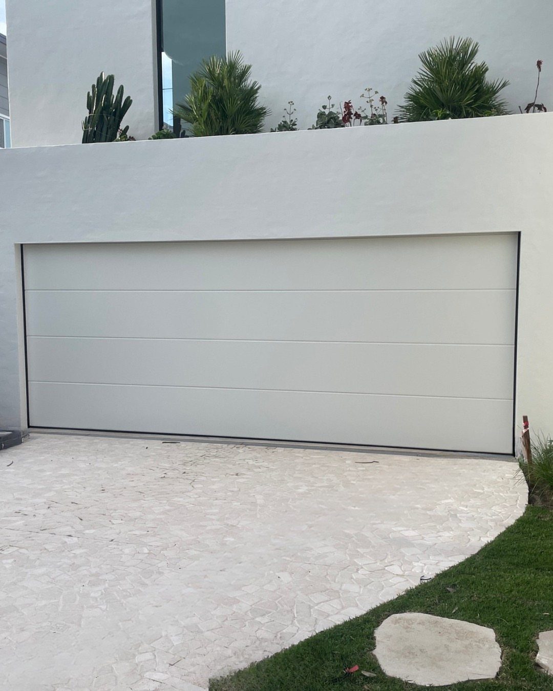 A modern white paneled garage door set into a white wall with a stone driveway.