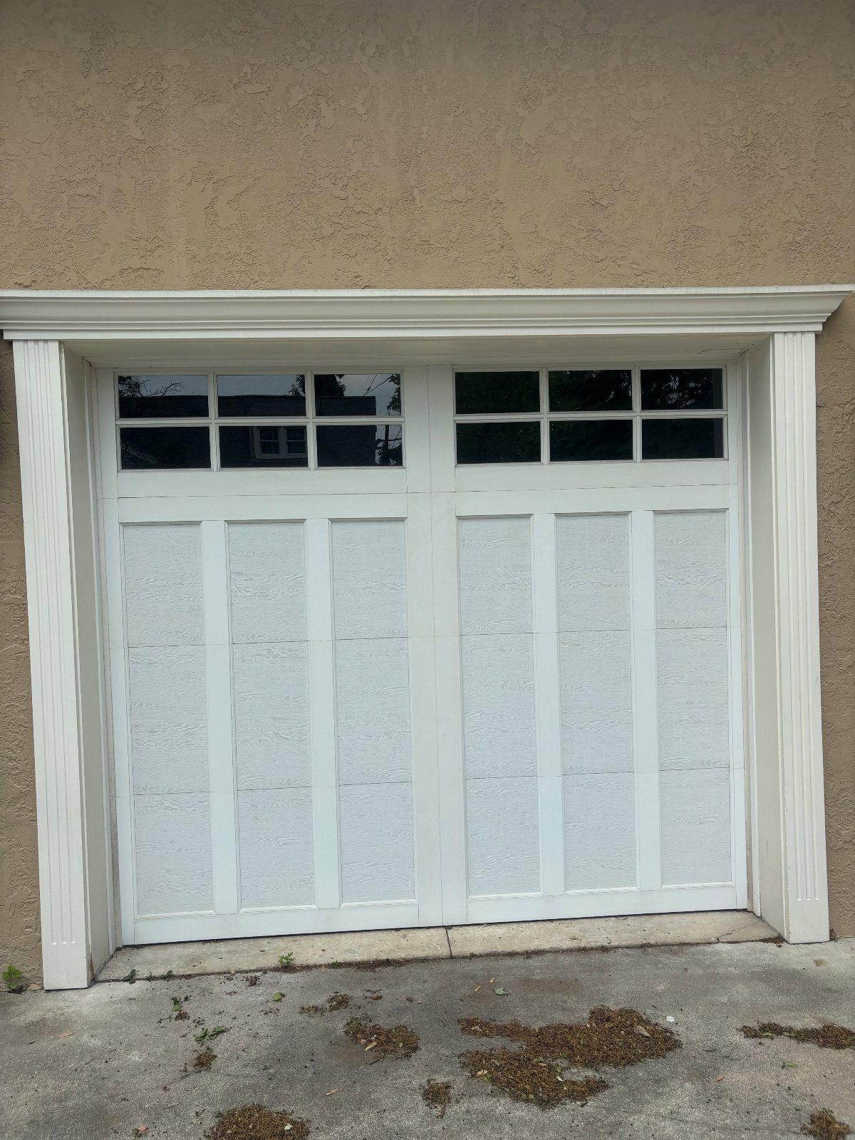 White garage door featuring a row of small window panes at the top against a tan wall.