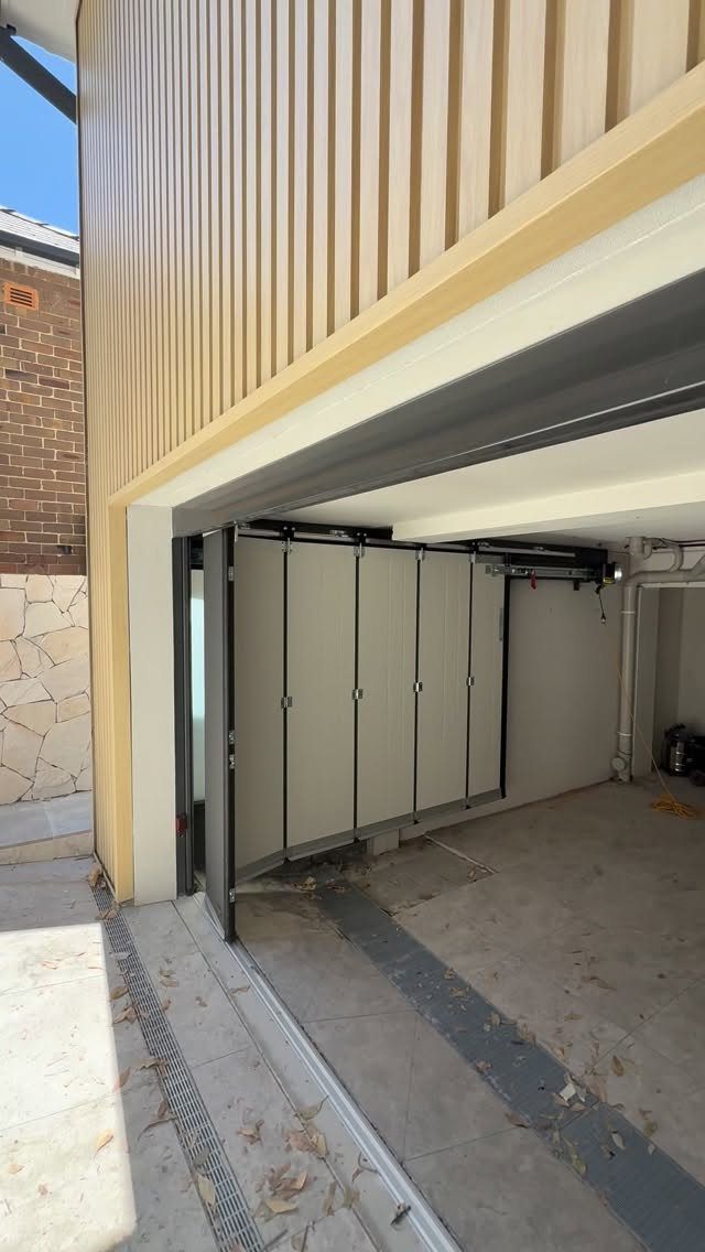 A modern folding garage door system partially opened in a light-colored garage space.