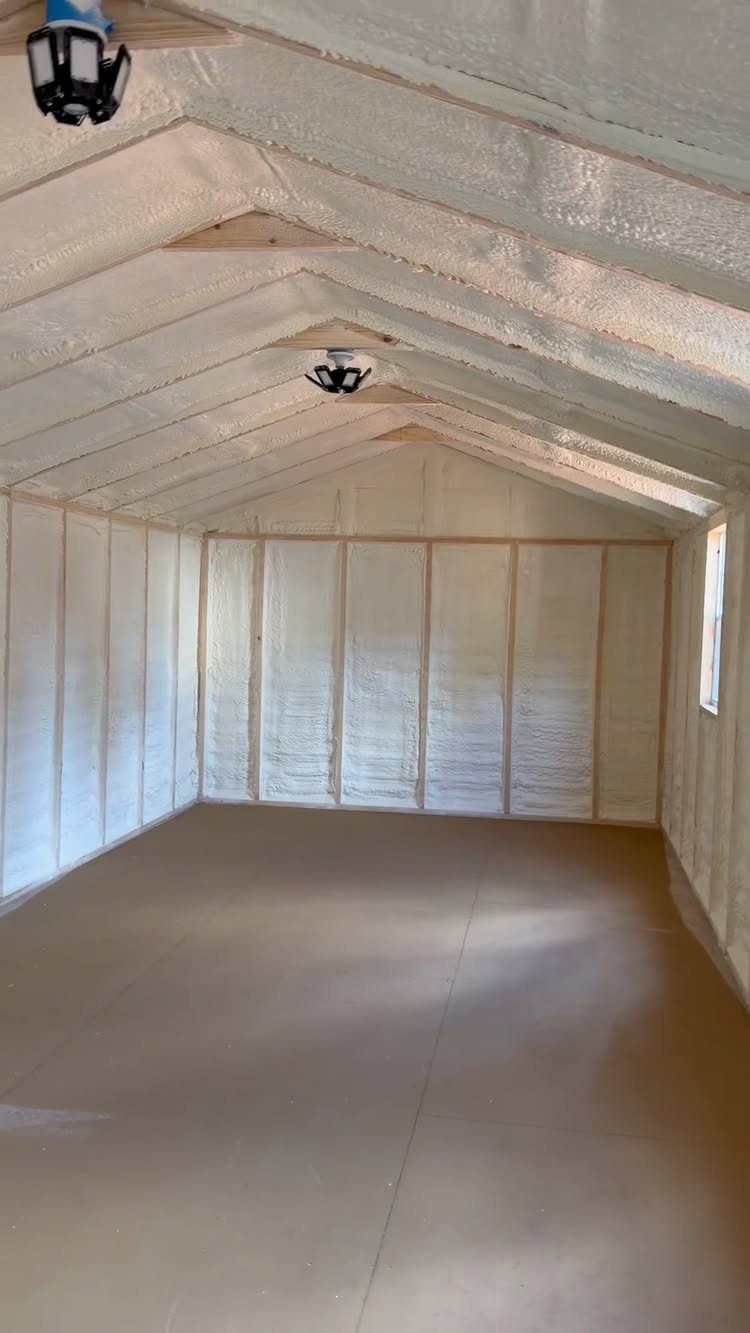 White spray foam insulation covering the walls and ceiling of a wooden shed interior.