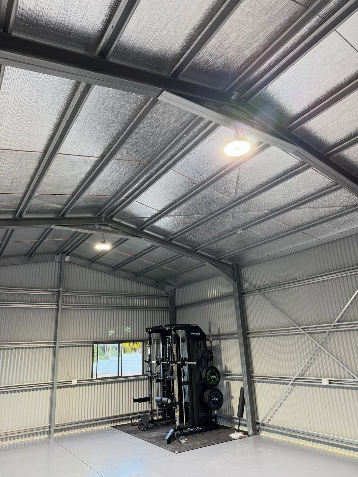 Metal shed gym interior featuring a power rack and bright circular LED ceiling lights.