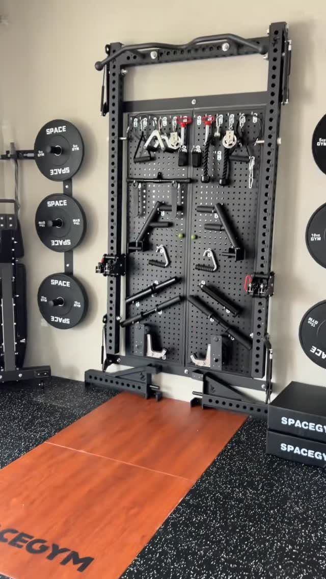 Black metal gym equipment rack with various attachments mounted on a wall above orange mats.