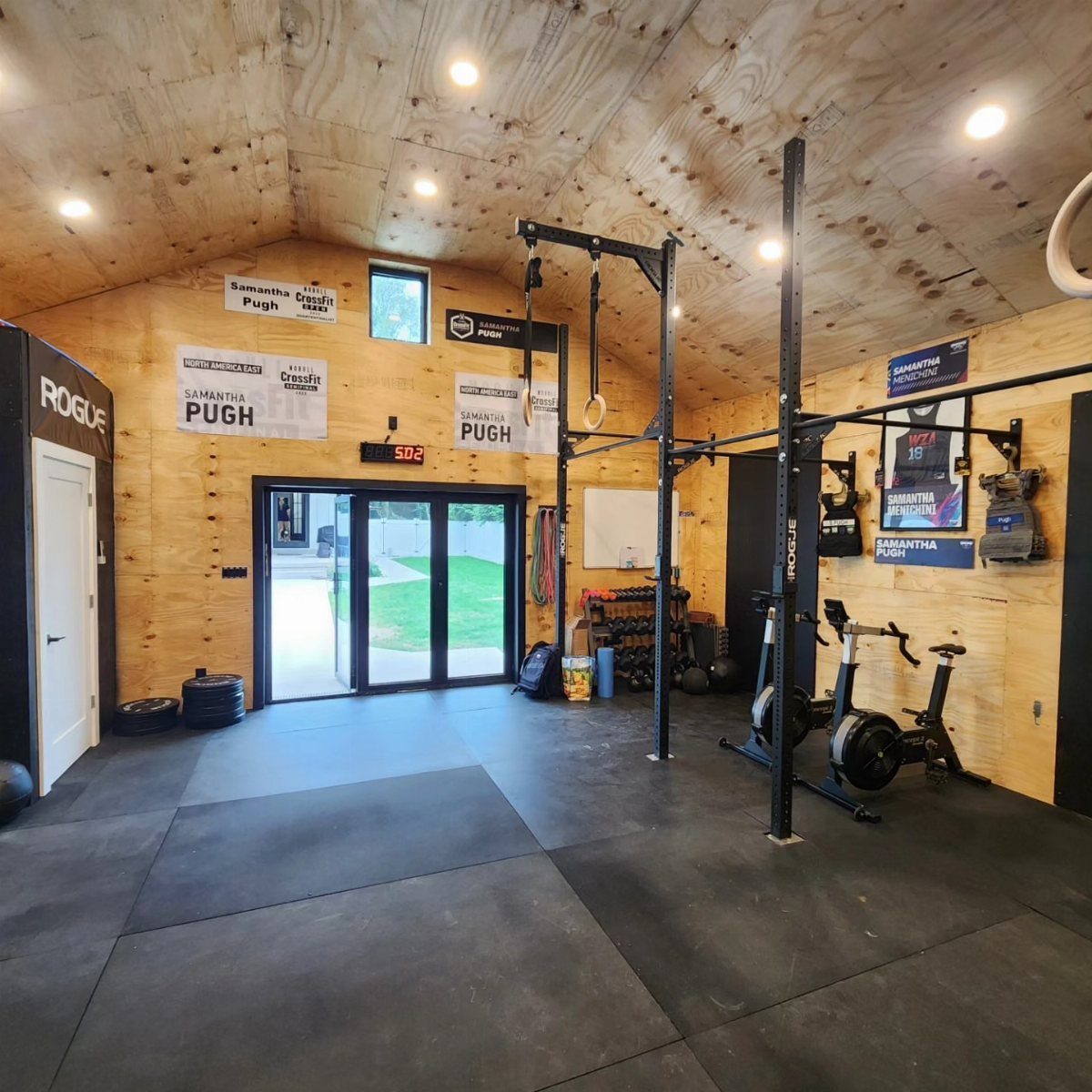 A wooden shed converted into a home gym with a power rack and stationary bike.